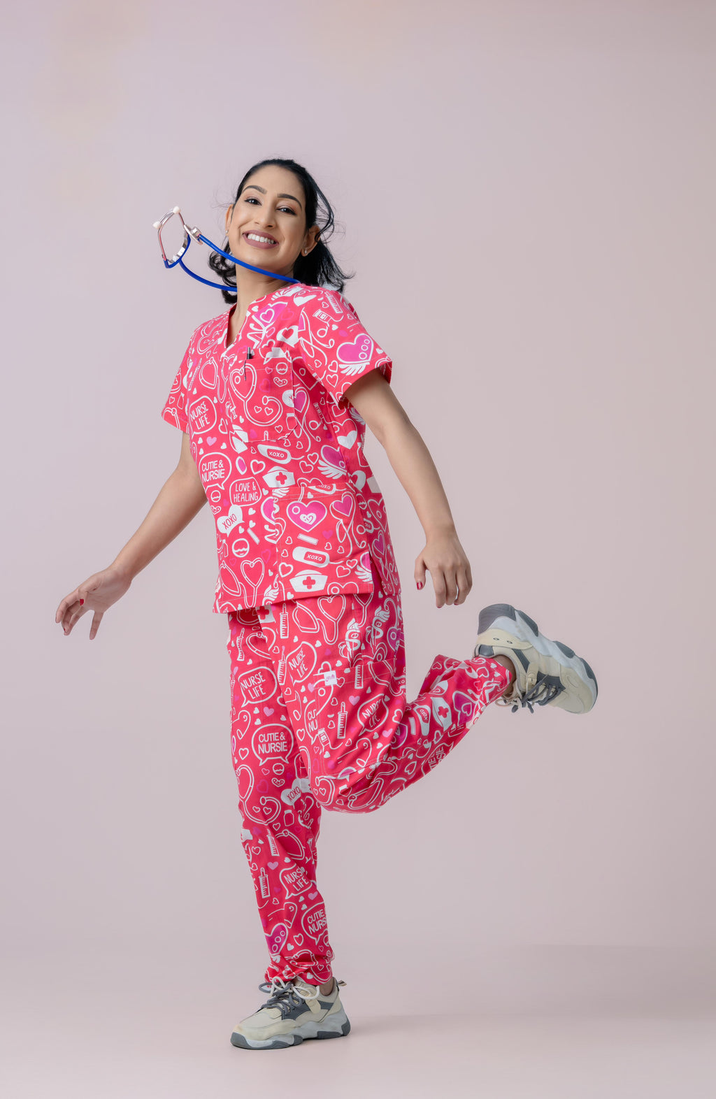 Female healthcare professional wearing pink heart print scrub uniform posing playfully